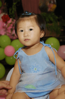 a little girl in a blue dress looks at the camera