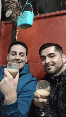 two men are toasting with wine glasses in front of a wall