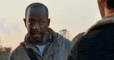 a man in a jacket is talking to another man in a field .