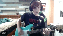 a boy wearing headphones and a nirvana shirt plays a guitar