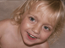 a young girl with blonde hair and blue eyes is smiling