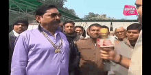 a man in a purple shirt is holding a microphone in front of a group of people and a sign that says bihar