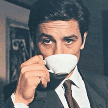 a man in a suit and tie is drinking from a cup