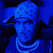 a man wearing a mask and a necklace has a blue background