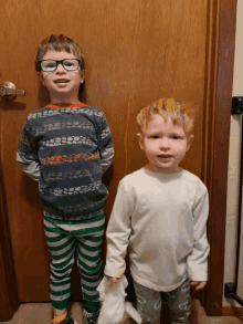 two young boys are standing next to each other in front of a wooden door