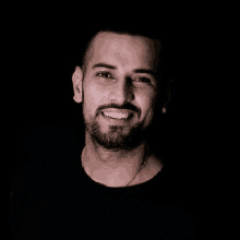 a man with a beard and earrings is smiling in a black background .