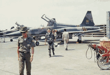 a man in a cowboy hat stands in front of a fighter jet with the numbers 3005 on the tail