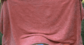 a man is laying on a lawn chair holding a pink towel over his face
