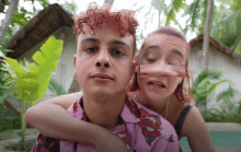 a man with curly hair is being hugged by a woman wearing a pink shirt with roses on it