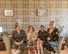 a group of women are sitting on a couch with confetti flying around them