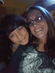 a woman wearing glasses and a bandana smiles next to another woman wearing a shirt with wings on it