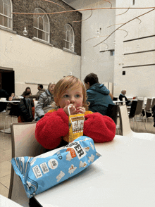 a little girl sitting at a table with a bag of popcorn and a carton of orange juice