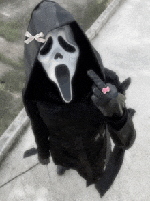 a person wearing a scream mask and a hooded jacket giving the middle finger