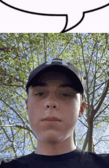 a young man wearing a hat and a black shirt stands in front of a tree