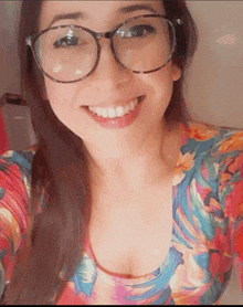 a woman wearing glasses and a colorful top smiles for the camera