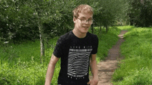 a young man wearing glasses and a black t-shirt is walking down a path .