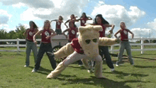 a group of women are dancing in a field with a mascot wearing sunglasses and a shirt that says oklahoma