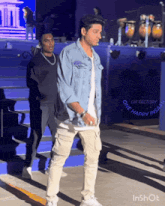 a man in a denim jacket is walking in front of a gif factory one happy insane logo