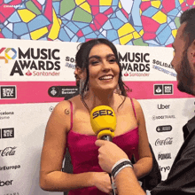 a woman in a pink dress is being interviewed by a man in front of a wall that says music awards