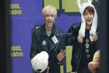 two young men are standing in front of an idol radio sign