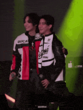 a man in a ducati jacket is hugging another man on stage