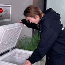 a man in a black hoodie with the word best on it looks into a freezer