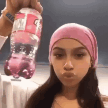 a woman wearing a pink headband is holding a pink bottle of soda in her hand .