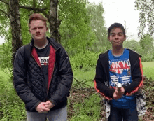 two young men are standing next to each other in a field . one of the men is holding something in his hand .