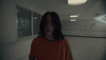 a woman in an orange shirt is standing in a dark room