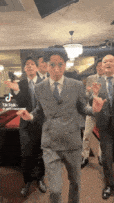 a group of men in suits and ties are dancing in a room .