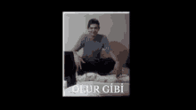 a man is sitting on a bed with the words olur gibi written on the bottom of the picture .