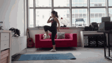 a woman stands on a yoga mat in front of a red couch with a sign on the wall that says fire escape and rescue