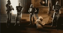 a group of stormtroopers are standing next to each other in a room with a man kneeling down .