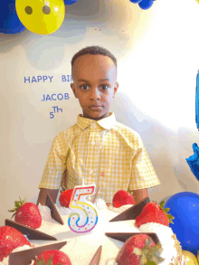 a young boy stands in front of a birthday cake with a candle in the shape of the number 5