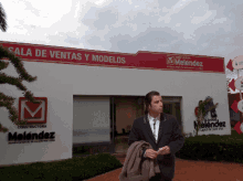 a man in a suit stands in front of a building that says sala de ventas y modelos on it