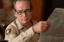 a man in a sheriff 's uniform is reading a newspaper while wearing glasses .