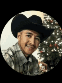 a man wearing a cowboy hat and plaid shirt is smiling in front of a christmas tree