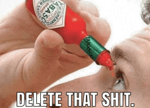 a person is holding a bottle of tabasco sauce in front of their eye .