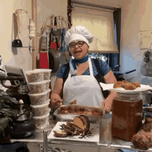 a woman wearing a chef 's hat and apron is standing in a kitchen holding a tray of food .