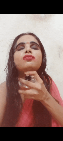 a woman spraying perfume on her face while wearing a red saree