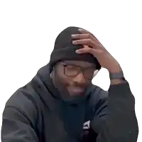 a man wearing a beanie and glasses holds his hand to his forehead