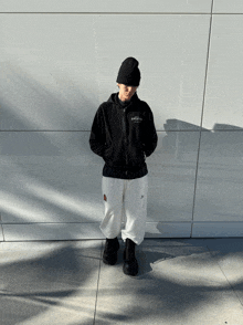 a person standing in front of a white wall wearing a black hoodie that says essentials on it