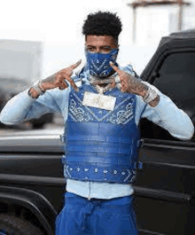 a man wearing a bandana and a blue vest is standing in front of a black car .