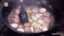 a pan filled with meatballs and vegetables is being stirred with a spatula .