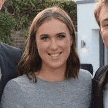 a woman in a grey shirt is smiling for the camera while standing next to two men .