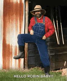 a man in overalls and a hat is standing in front of a barn and saying hello robin baby .