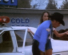 a man in a cowboy hat is standing next to a police car in front of a sign that says " cold "