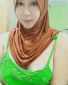 a woman wearing a hijab and a green tank top is standing in a room .