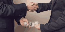 a man in a suit shakes hands with another man holding a 100 dollar bill