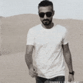 a man wearing sunglasses and a white t-shirt is standing in the desert